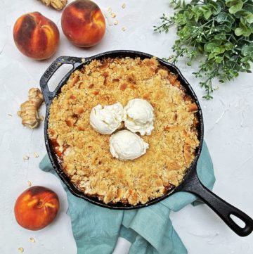 Ginger peach crisp in a cast iron skillet surrounded by peaches and flowers