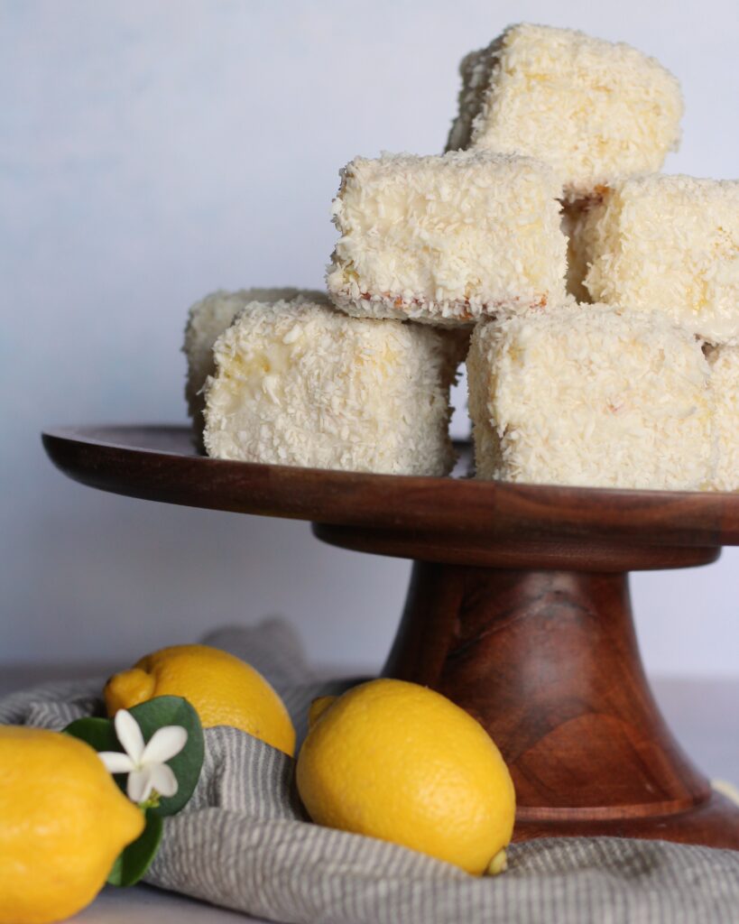 Pile of lemon white chocolate lamingtons on a cake stand with lemons. 